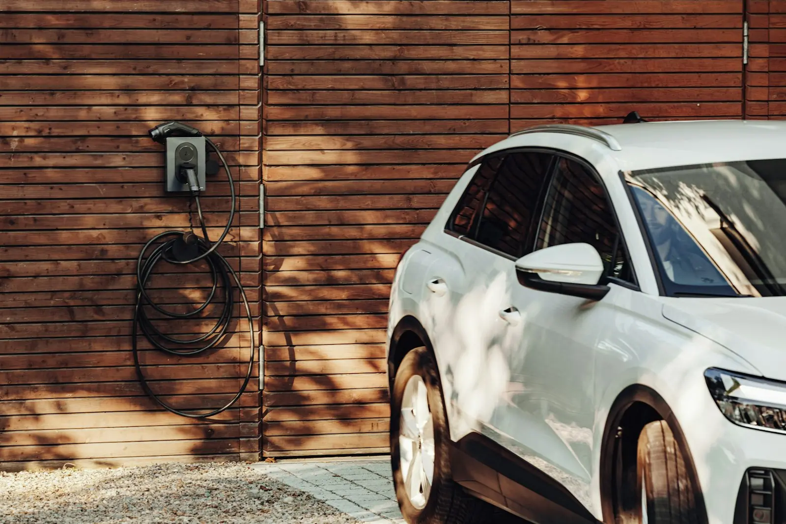 Witte elektrische auto naast een laadpaal aan een houten gevel