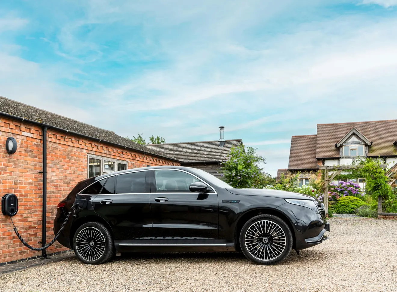 Elektrische auto laadt aan een laadpaal op de gevel van een bakstenen huis