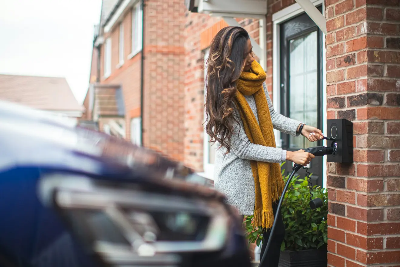 Vrouw sluit haar elektrische auto thuis aan op de laadpaal aan de gevel