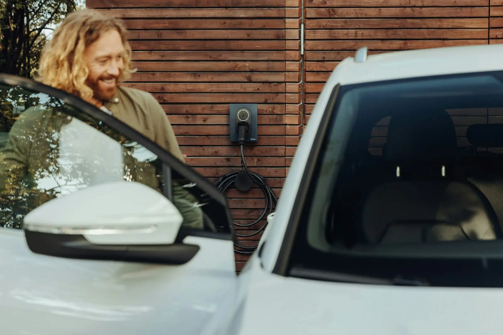 Man stapt in zijn elektrische auto die thuis aan de laadpaal staat