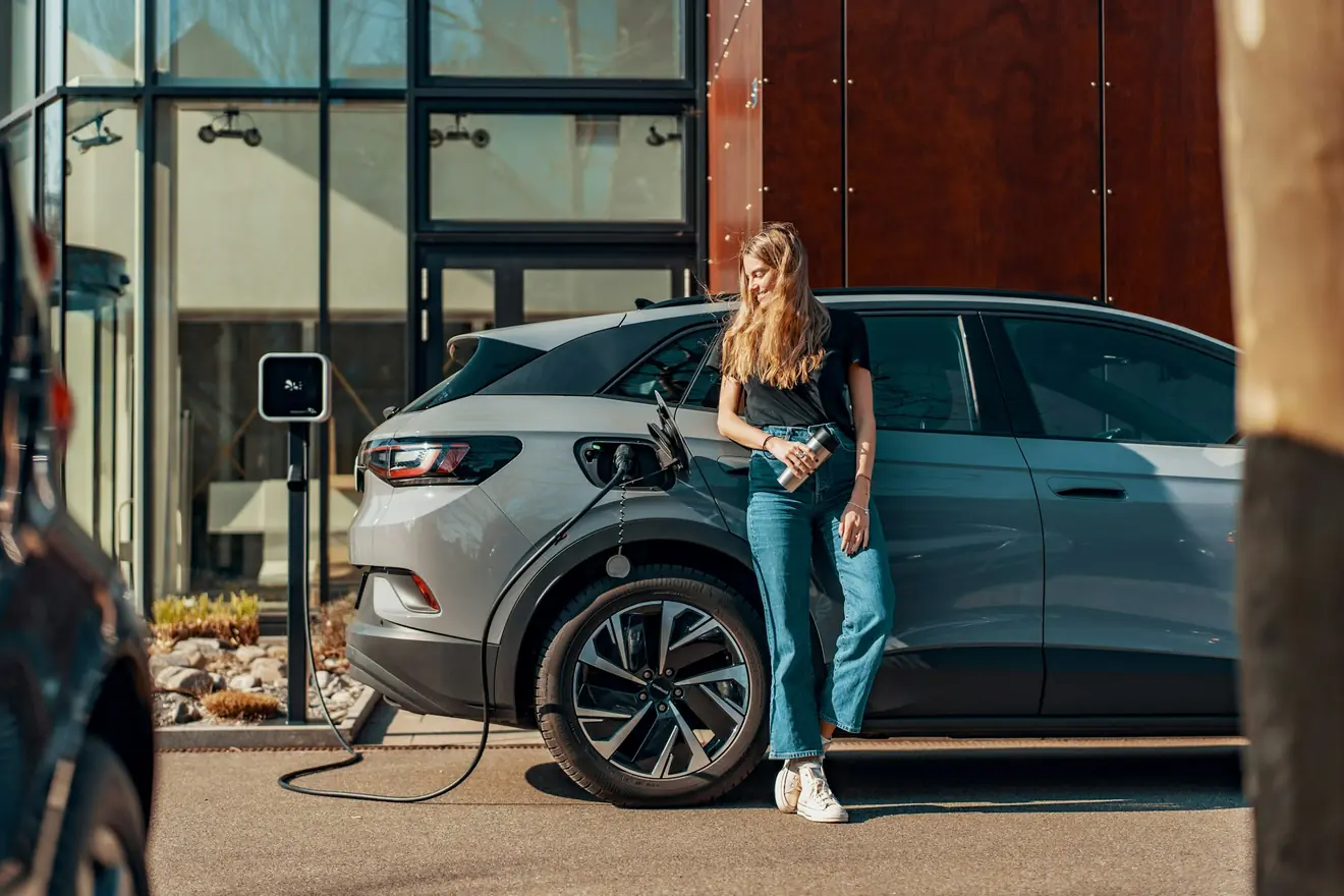 Vrouw staat bij haar elektrische auto die voor haar huis aan de laadpaal hangt