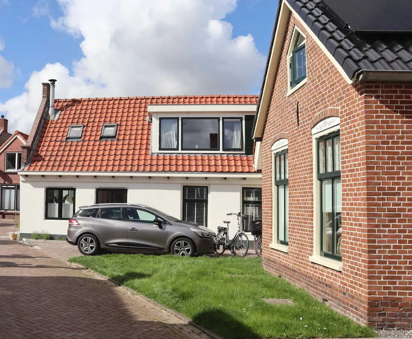 Grijze auto geparkeerd voor een wit huis met een rood pannendak, met twee fietsen ernaast